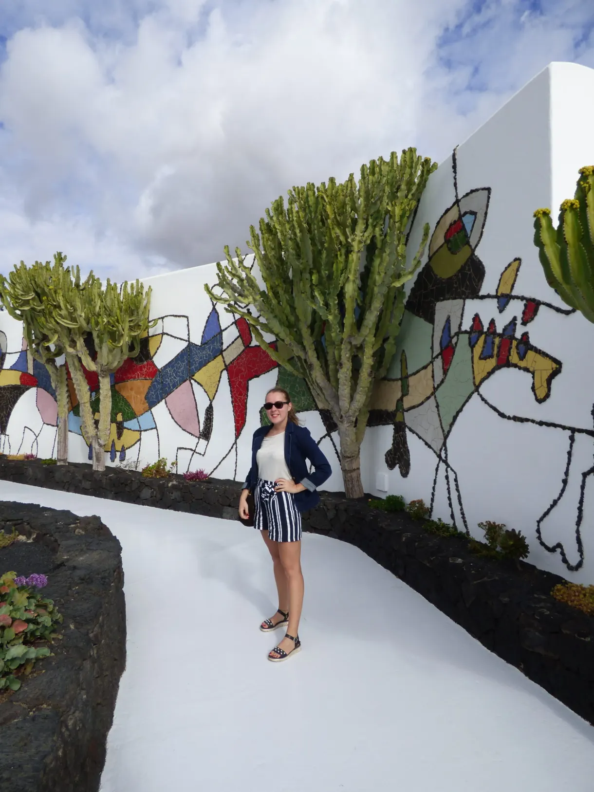 Visiteuse devant une fresque colorée entourée de cactus