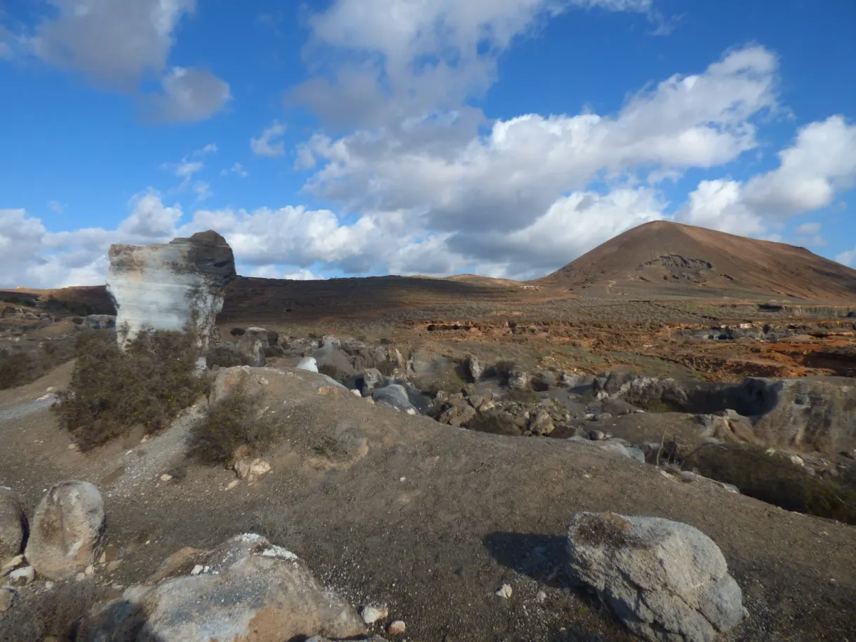 Blocs de roche claire et cône volcanique brun sous les nuages