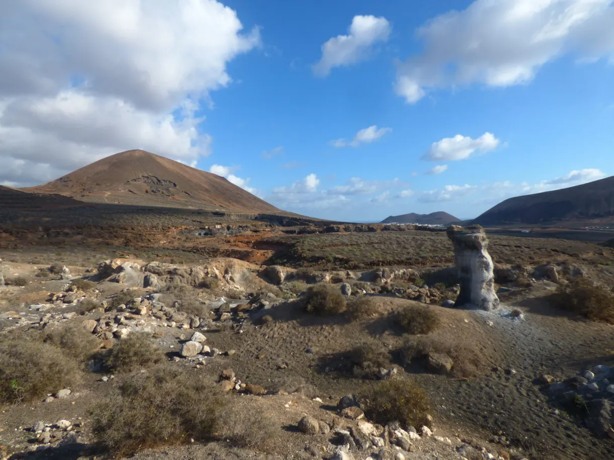 Cheminée de pierre blanche dressée devant un volcan brun