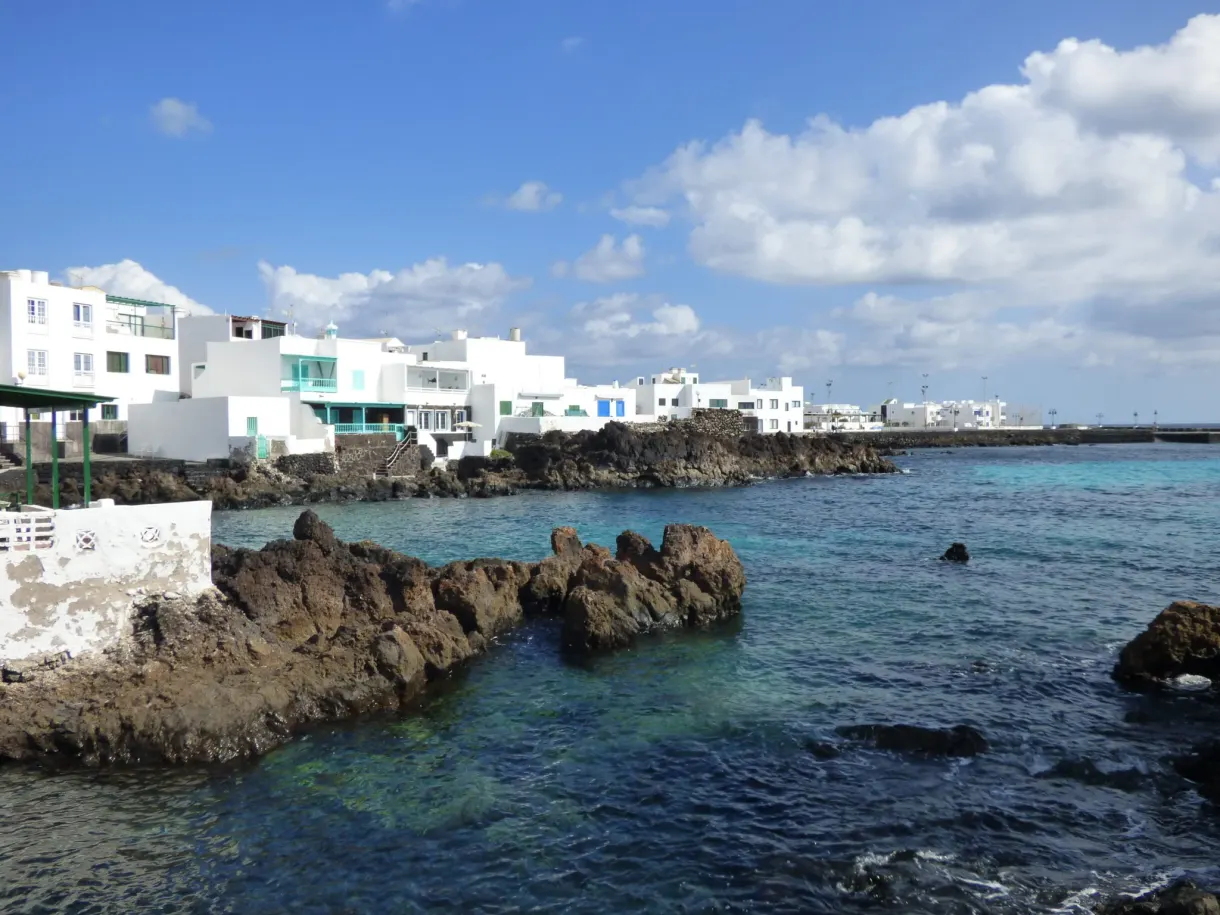Maisons blanches derrière des roches noires et une eau turquoise