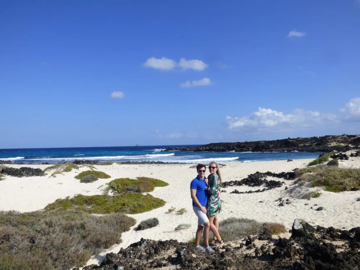 Couple posant sur une plage blanche bordée de roche noire