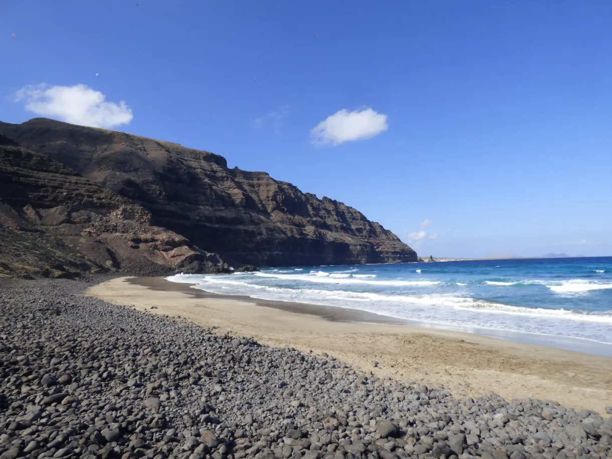 Plage de galets sombres au pied d'une haute falaise brune