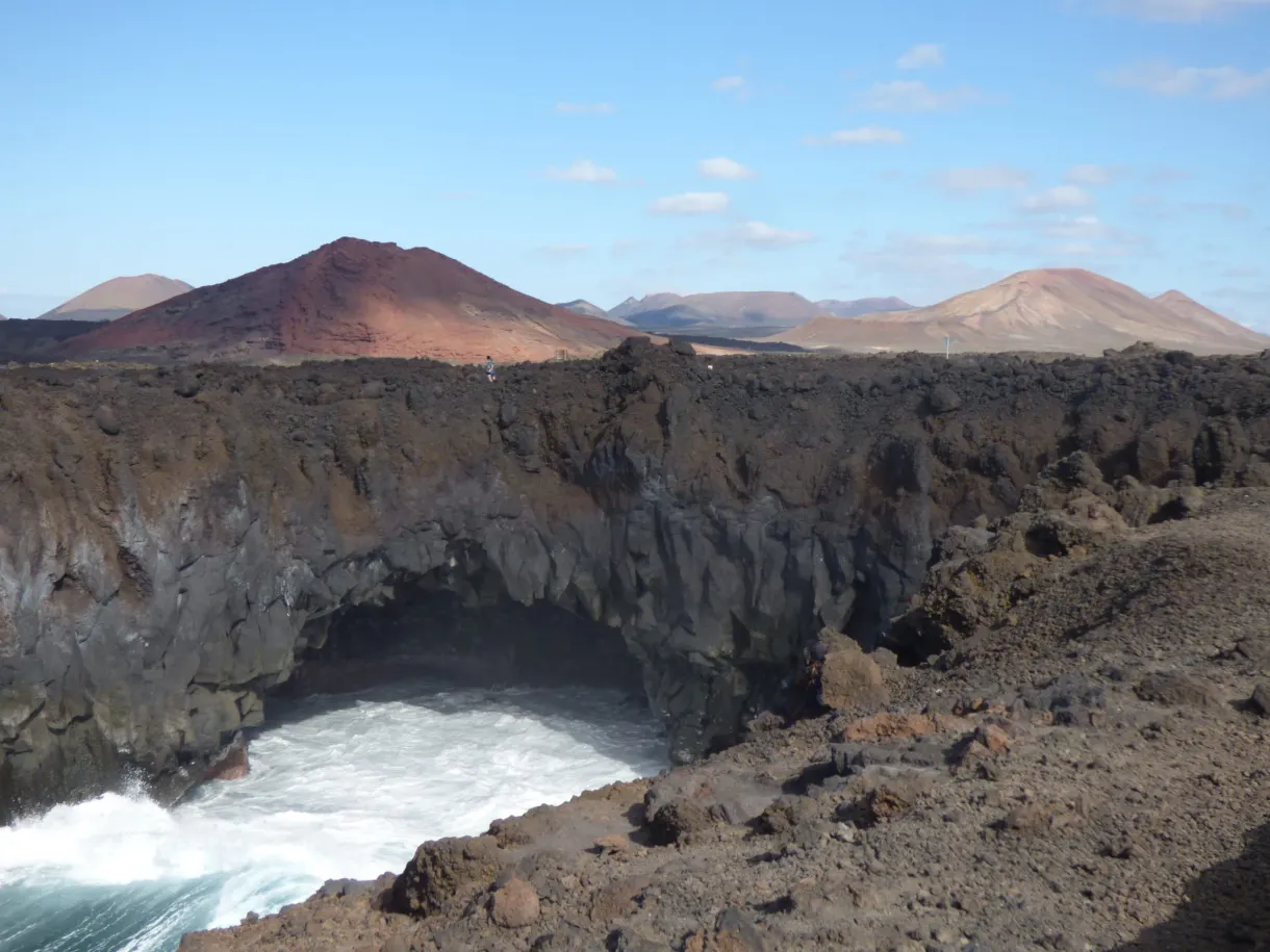 Arche de lave creusée par la mer, volcans rouges derrière