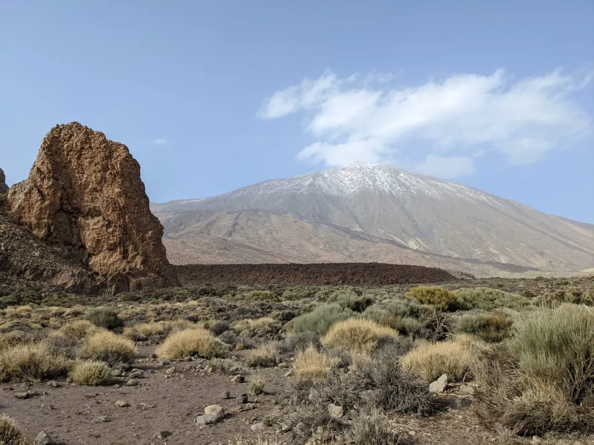 Ochre rock needle facing the snow-capped volcano