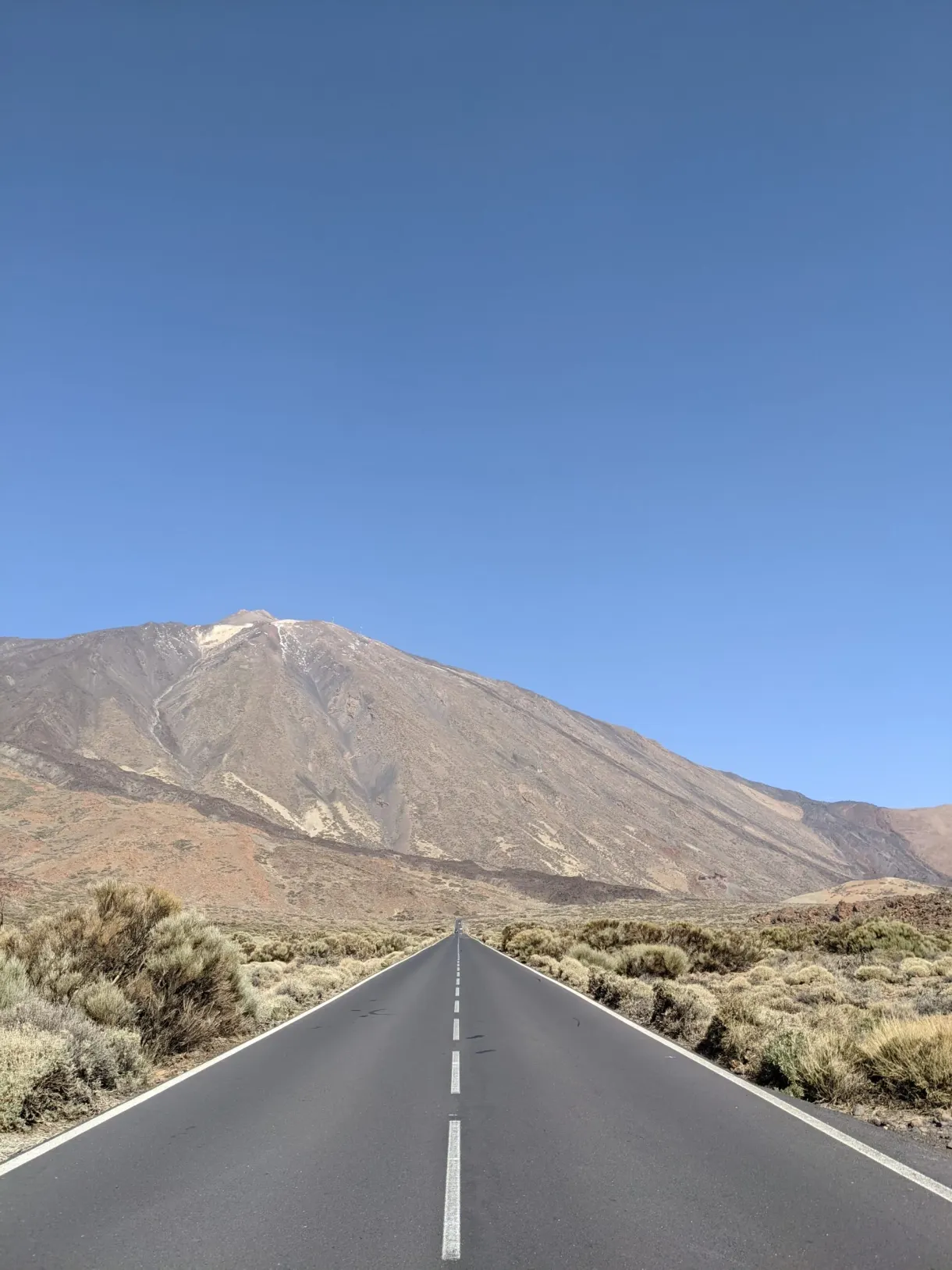 Straight road running towards the volcano under a blue sky