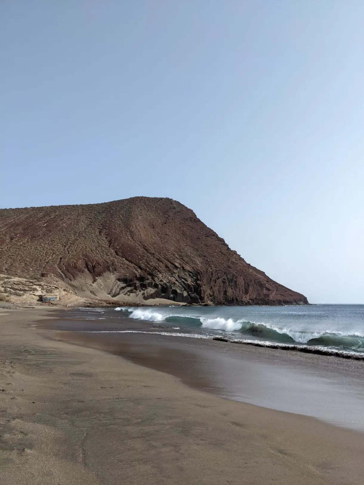 Plage de sable sombre au pied d'une colline rouge
