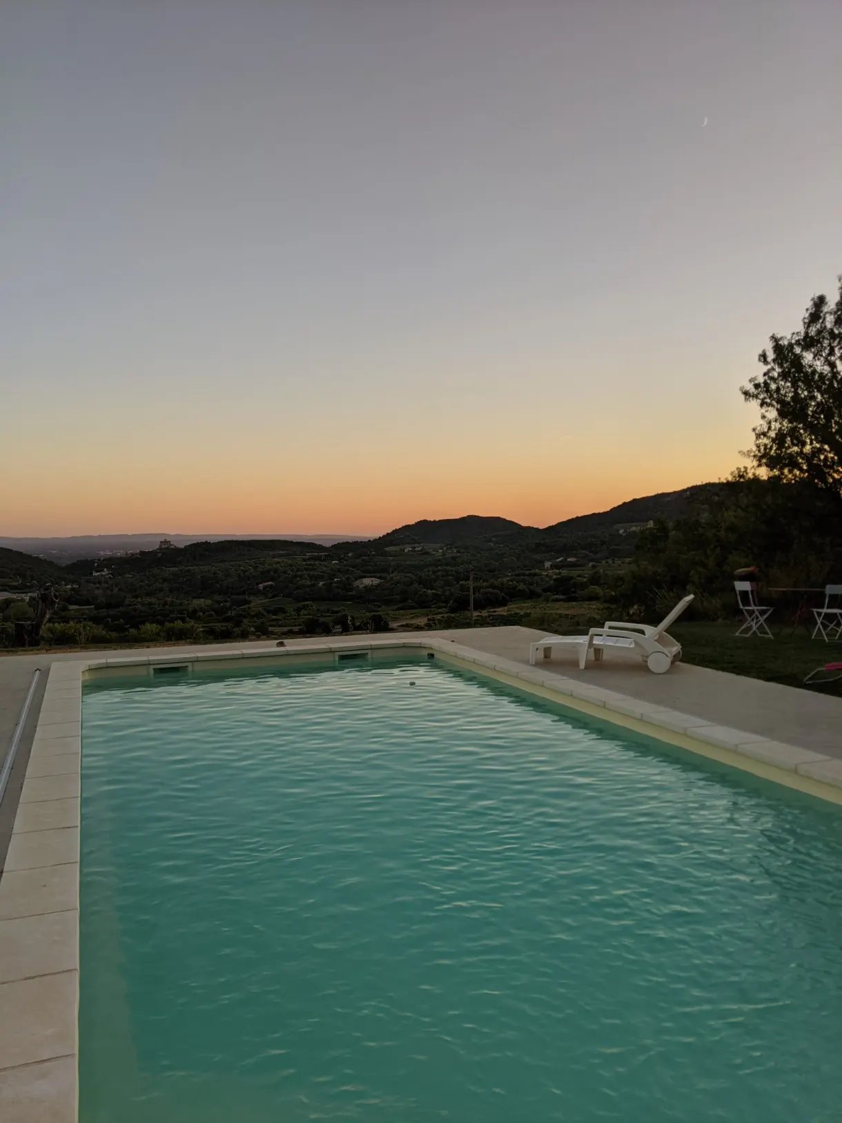 Piscine turquoise et transats face au ciel orangé du crépuscule