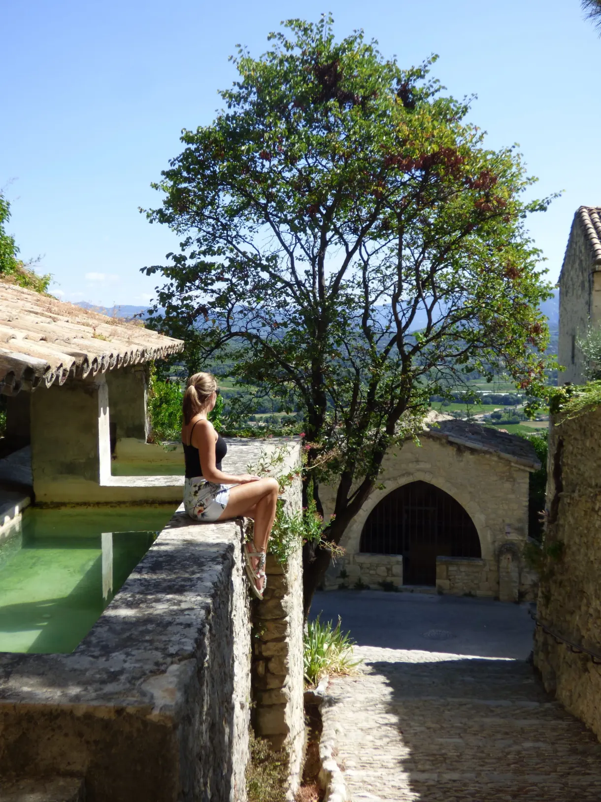 Femme assise au bord du lavoir ancien, vallée en contrebas