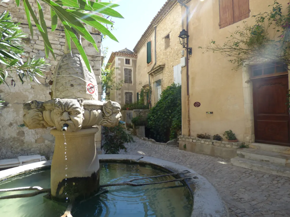 Fontaine à mascarons et son bassin rond dans une ruelle pavée