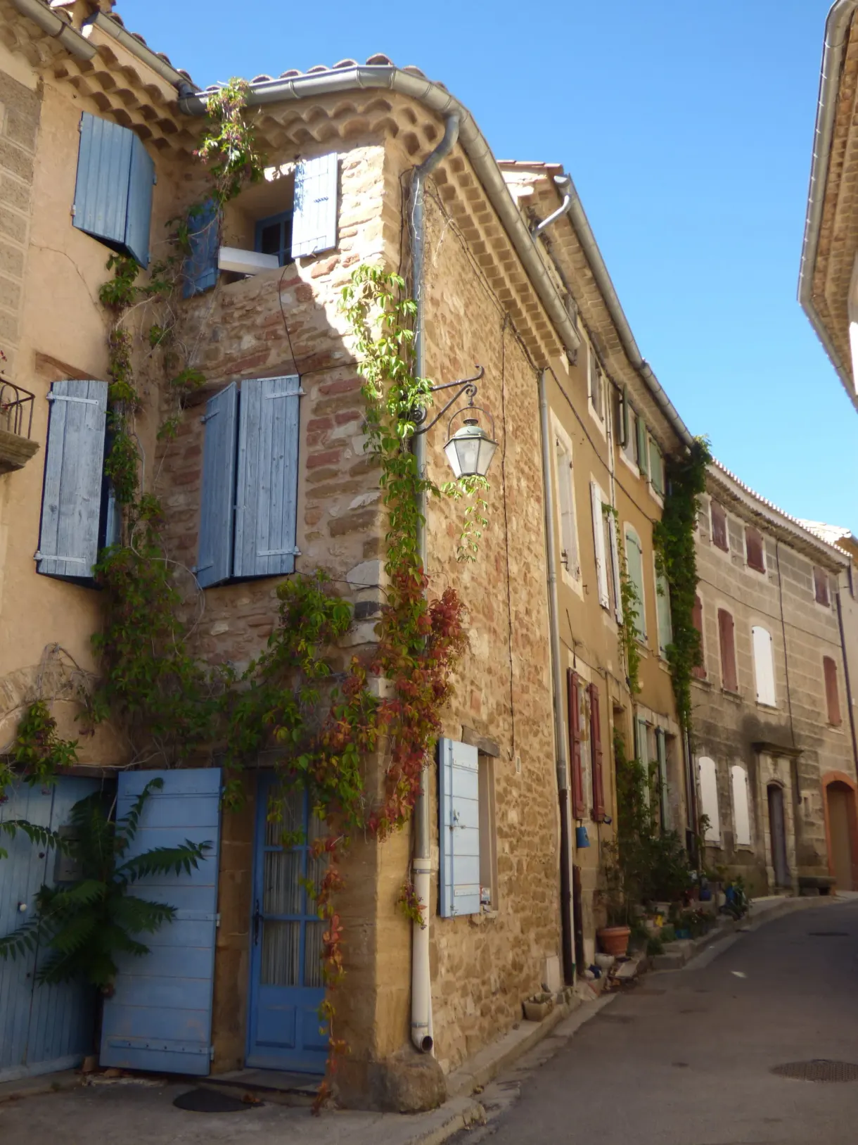 Maison d'angle en pierre dorée, volets bleus et lanterne