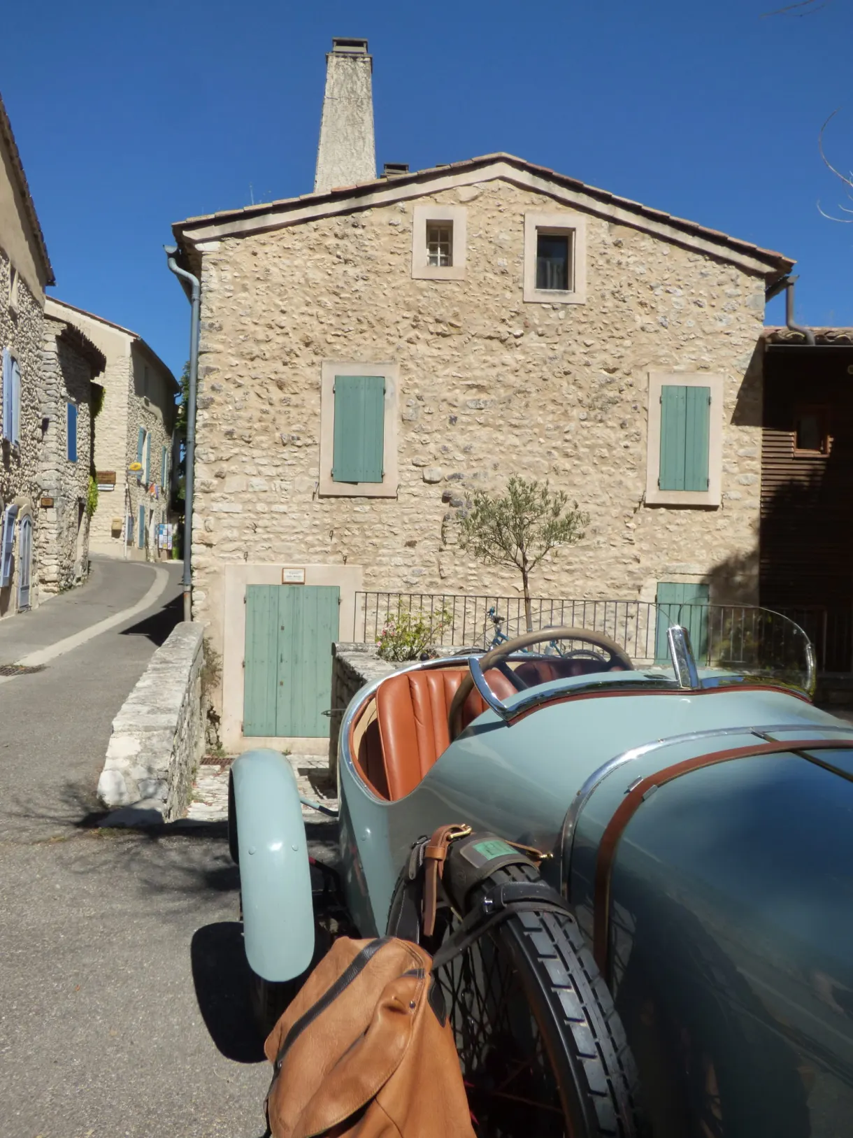 Voiture de collection bleue garée devant une maison de pierre