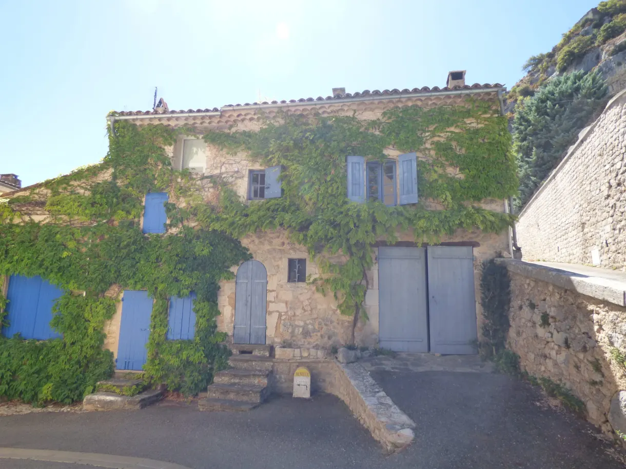 Maison de pierre envahie de vigne vierge sous la falaise