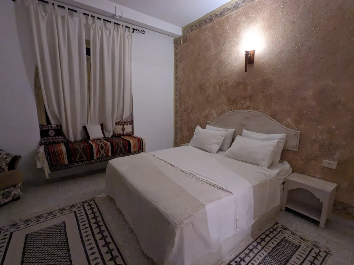 Chambre chez Mabrouk et Fatma à Tataouine, grand lit blanc et banquette aux coussins berbères