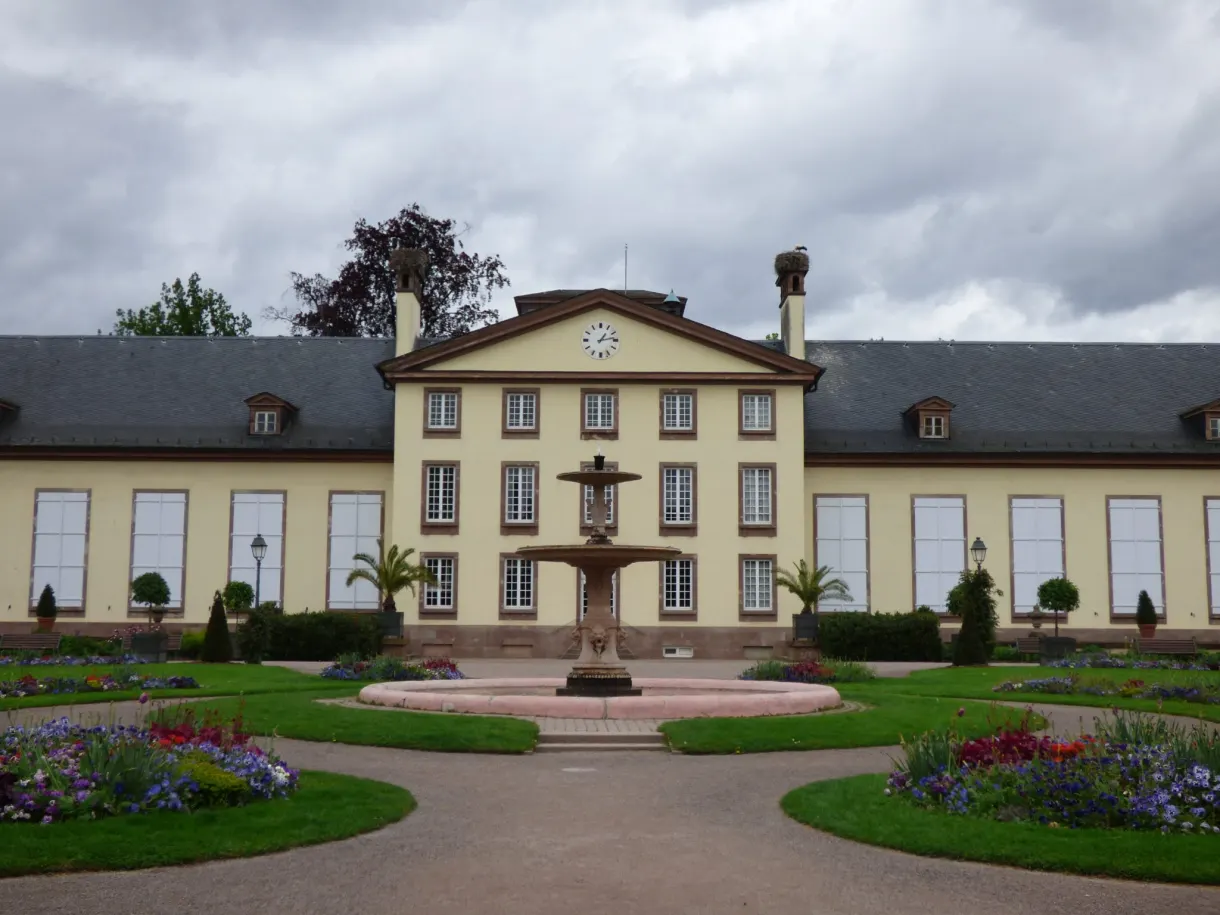 Bâtiment néoclassique jaune et fontaine ronde au centre du parc