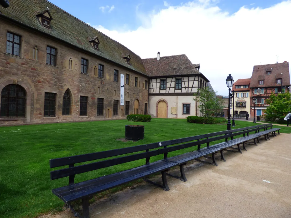 Cour close bordée de bâtiments anciens et de bancs alignés