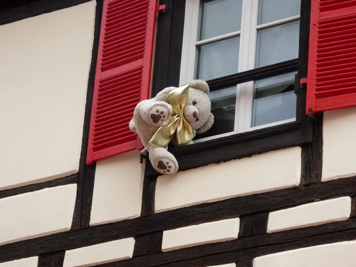 Ours en peluche posé sur un rebord de fenêtre à volets rouges
