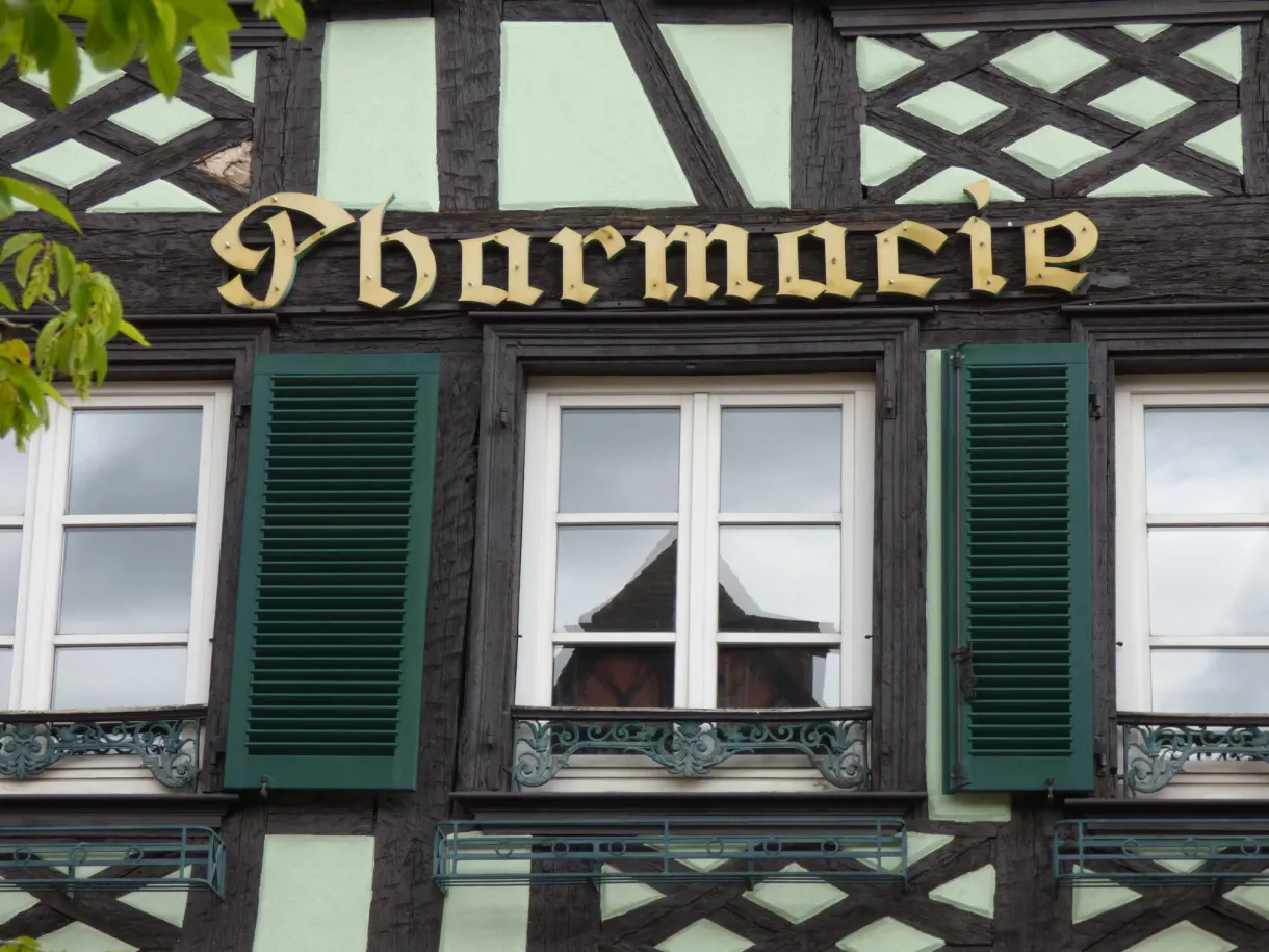 Enseigne dorée de pharmacie sur une façade à pans de bois