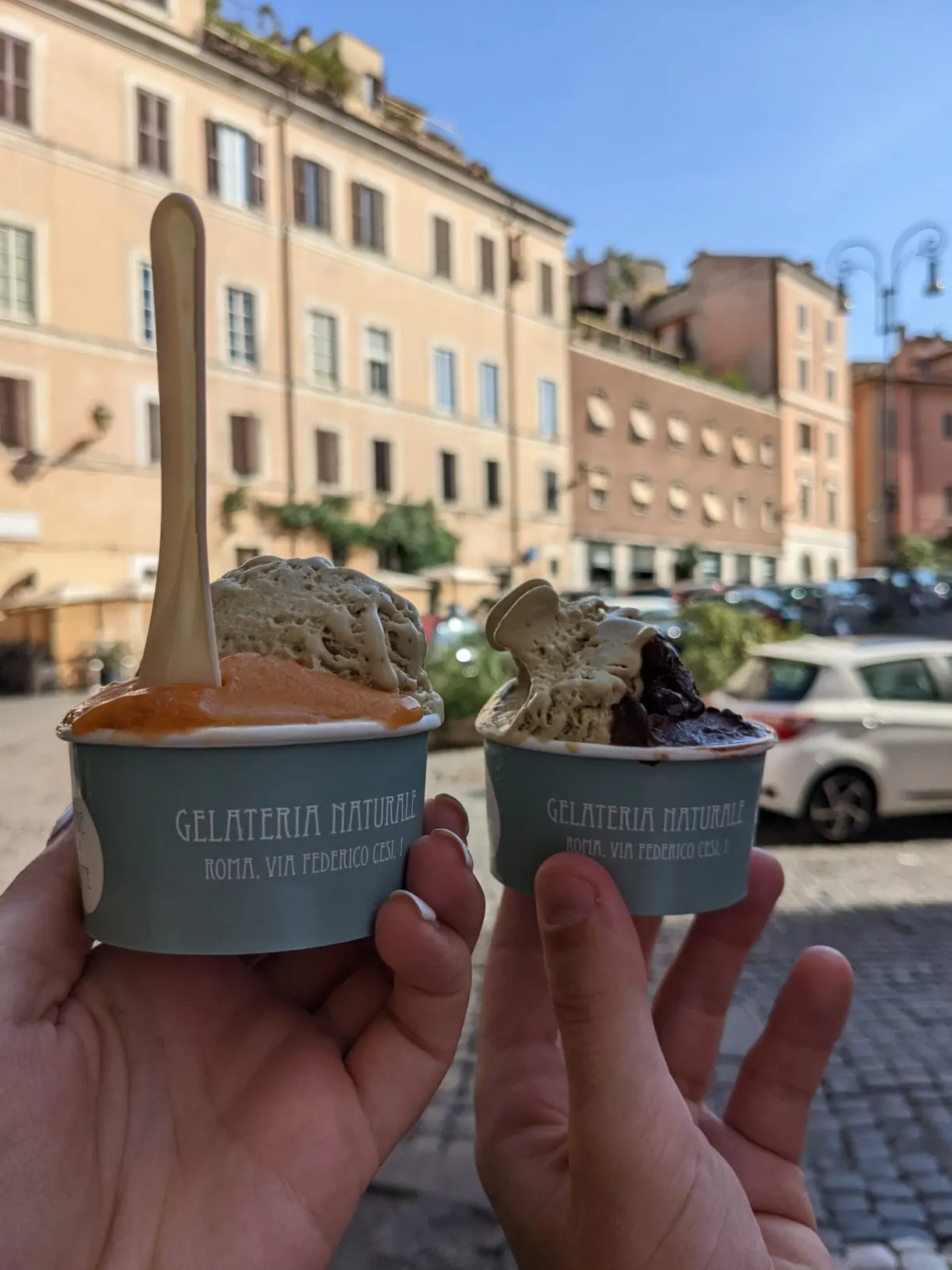 Deux pots de glace tenus devant une place ensoleillée