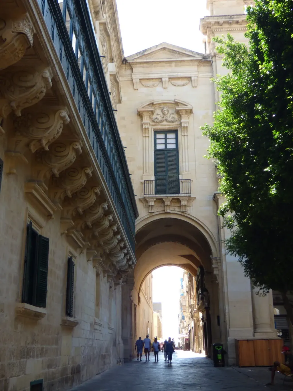 Ruelle passant sous une arche, balcons ouvragés et arbre vert