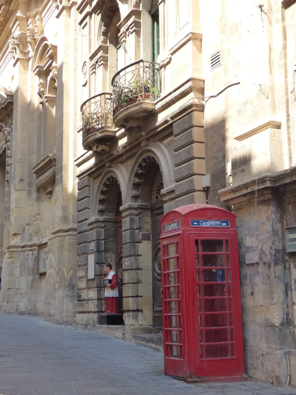 Cabine téléphonique rouge au pied d'une façade à balcons de pierre