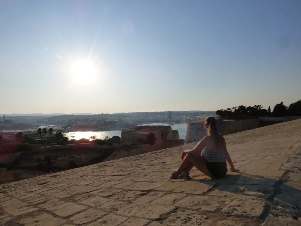 Femme assise sur le rempart face au soleil couchant