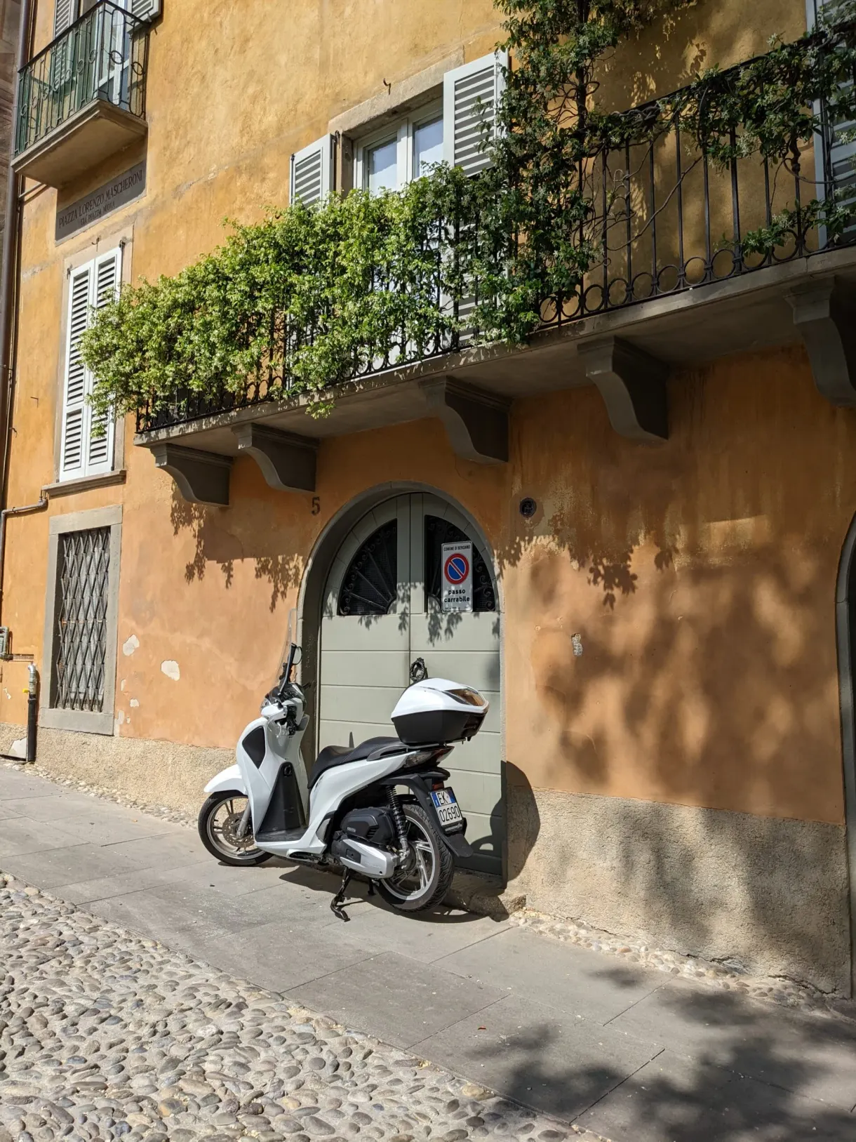 Scooter blanc garé sous un balcon fleuri de façade ocre