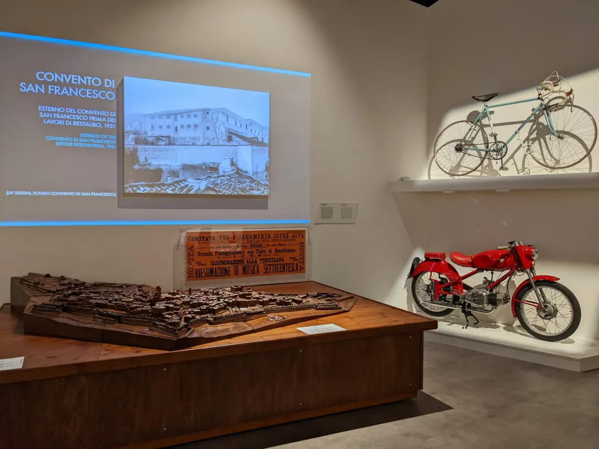Salle d'exposition avec maquette de bois et cyclomoteur rouge