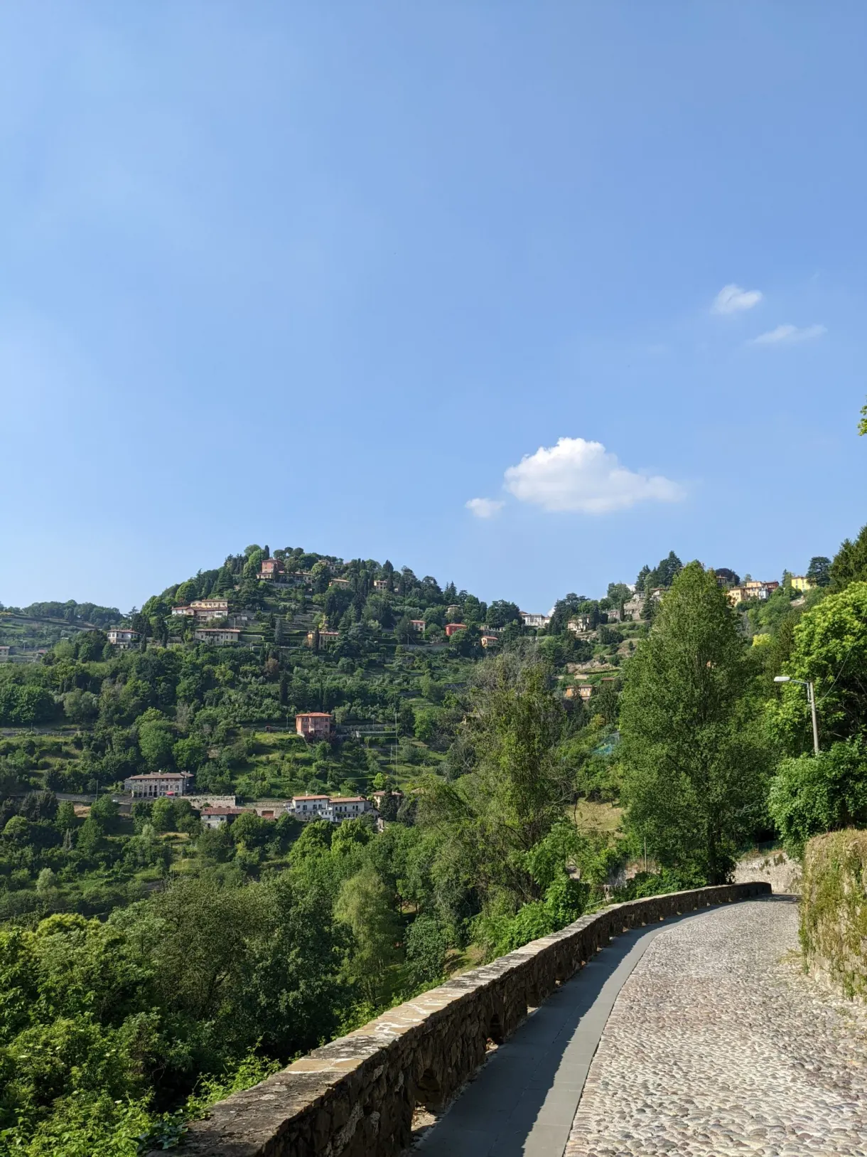 Chemin pavé longeant un mur face à une colline habitée