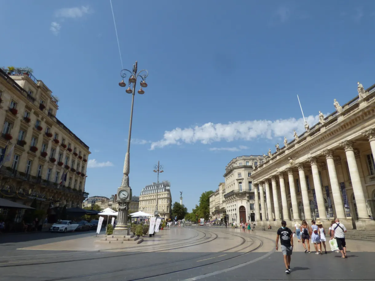 Place de la Comédie traversée par des passants sous un ciel bleu