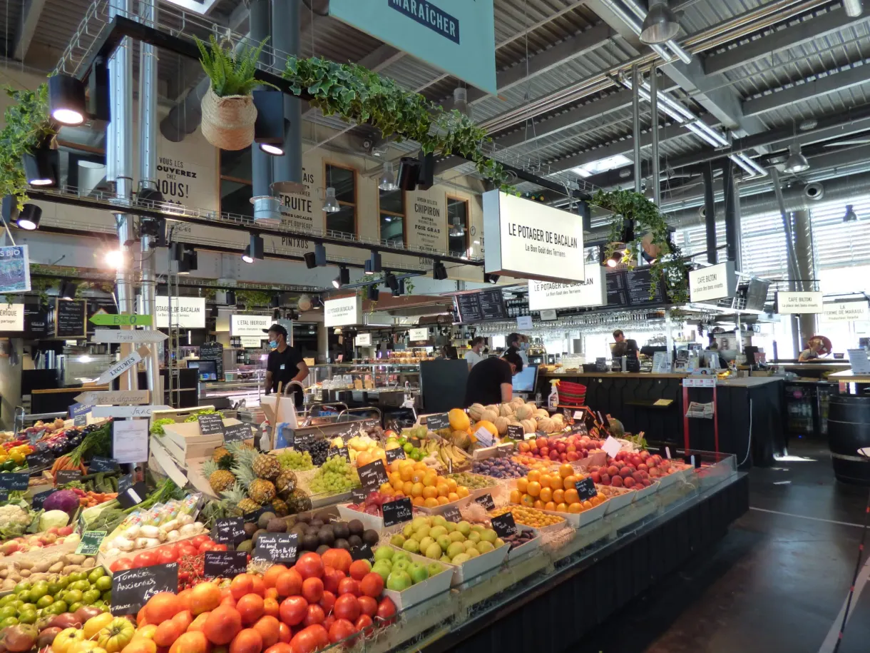 Étal coloré de fruits et légumes sous la verrière d'une halle