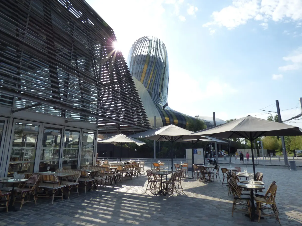 Terrasse de tables et parasols au pied d'un bâtiment de verre courbe