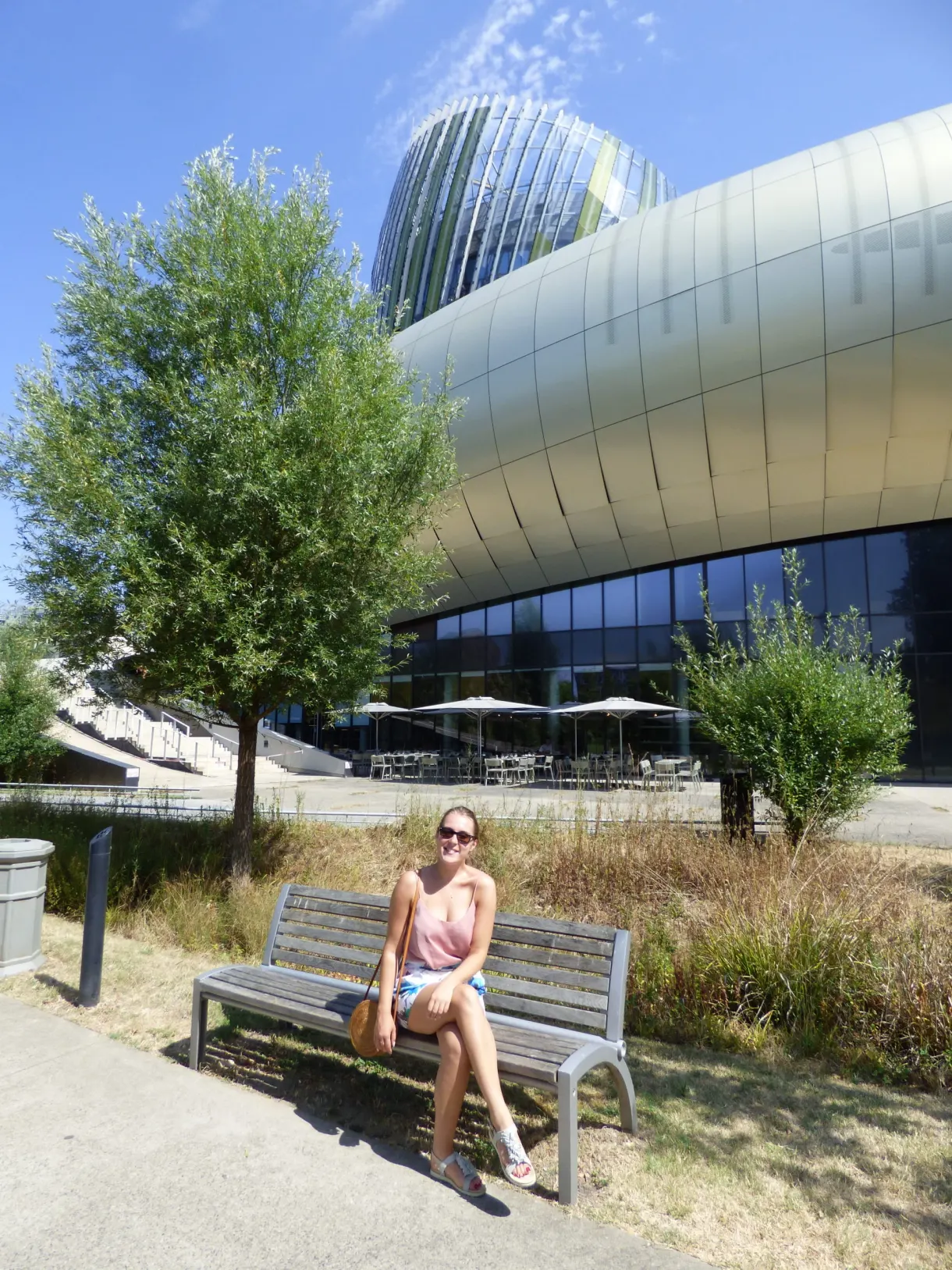 Femme assise sur un banc devant une architecture métallique ondulée
