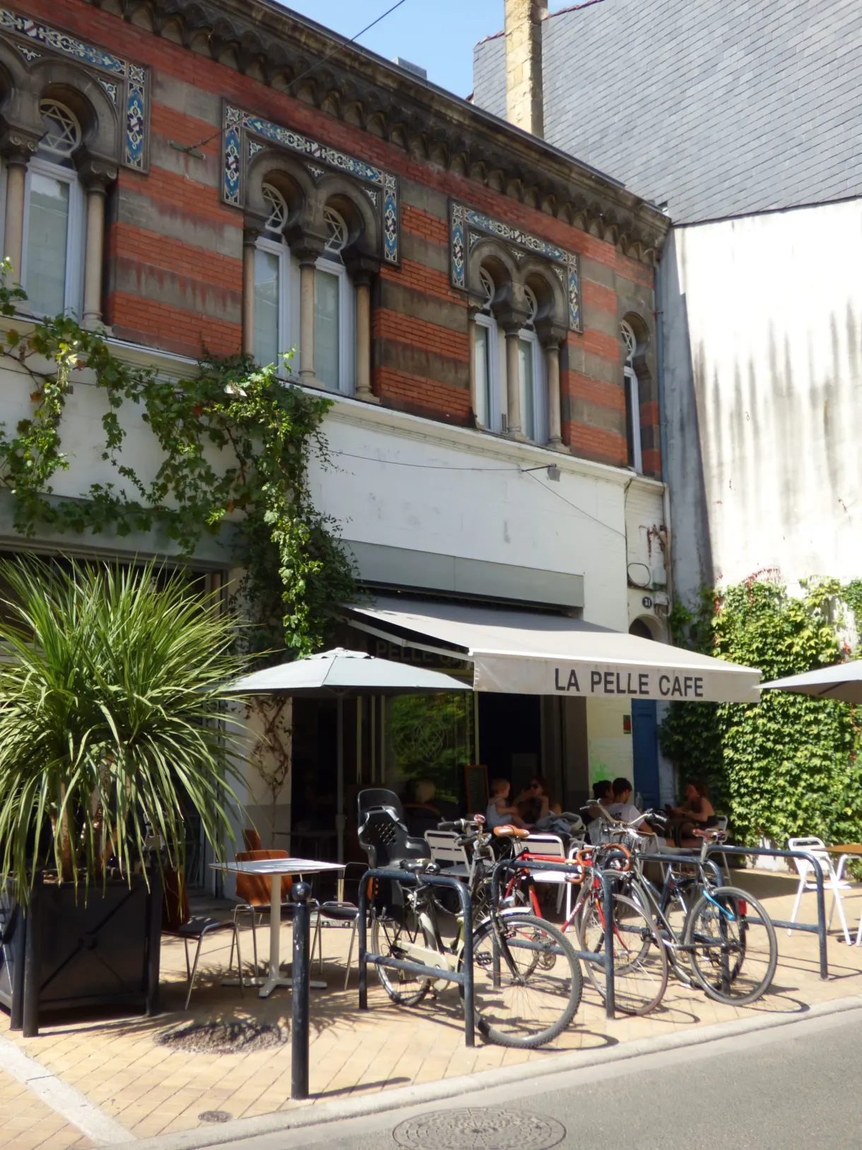 Terrasse de café sous store blanc devant une façade de brique rouge