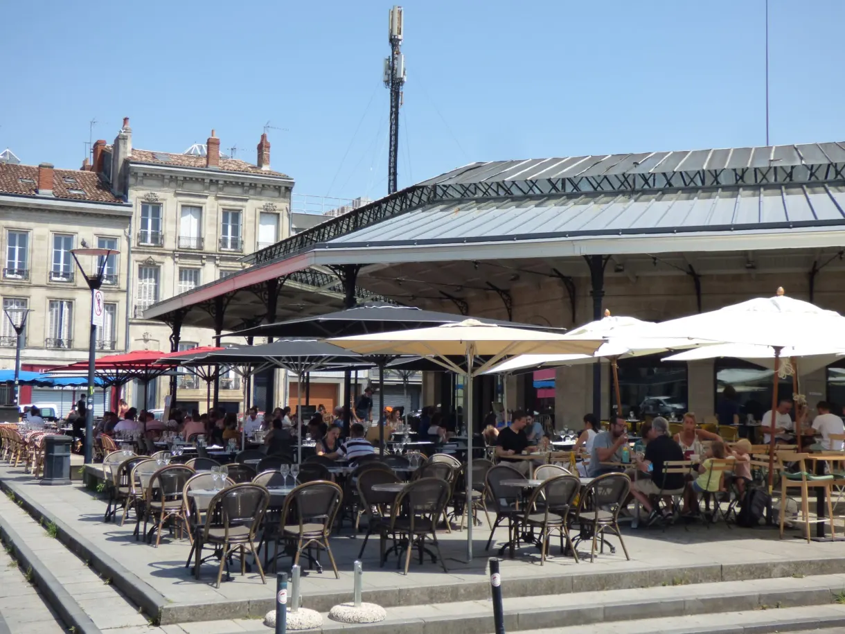 Terrasses bondées sous la halle métallique d'un marché de quartier