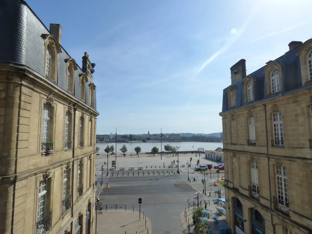 Place et fleuve aperçus en hauteur entre deux façades de pierre
