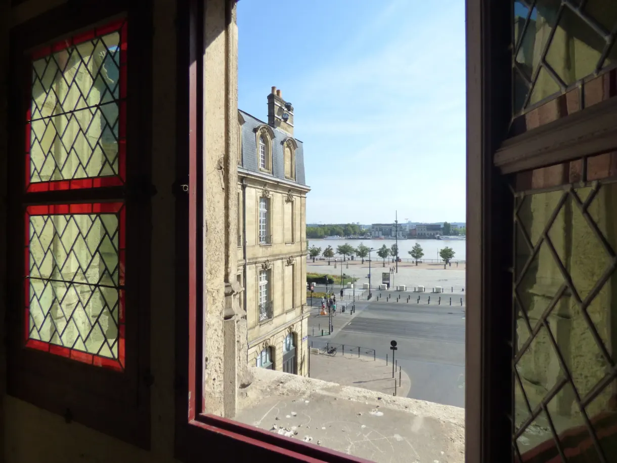Fenêtre à vitraux rouges ouverte sur la place et les quais