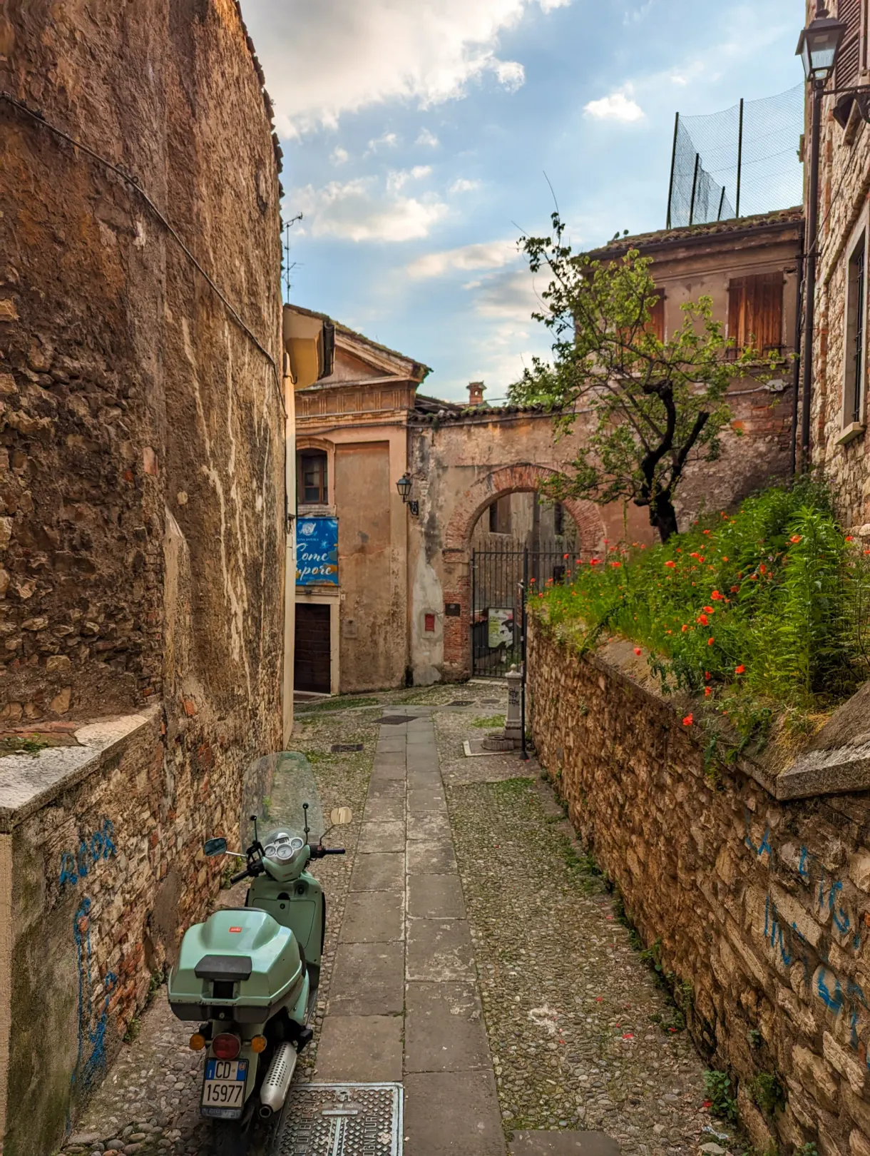 Scooter vert garé dans une ruelle pavée en pente
