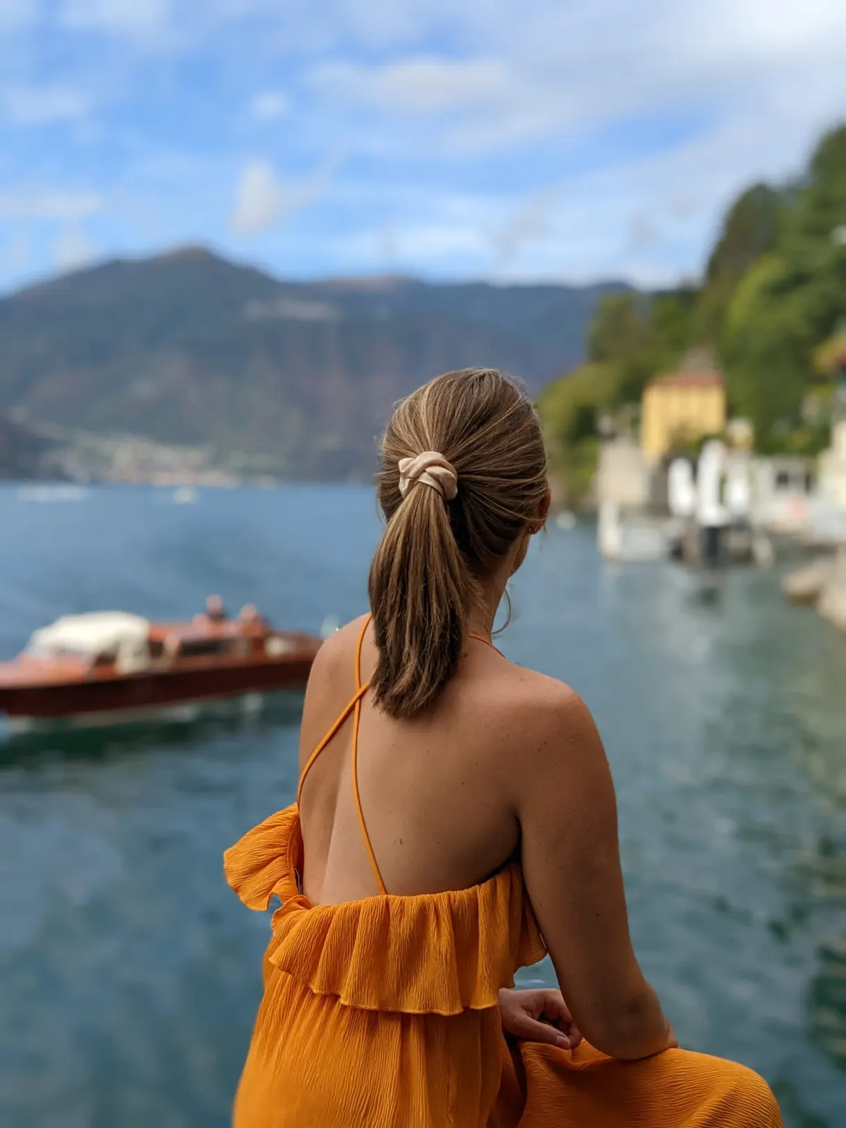 Femme en robe orange regardant passer un canot en bois