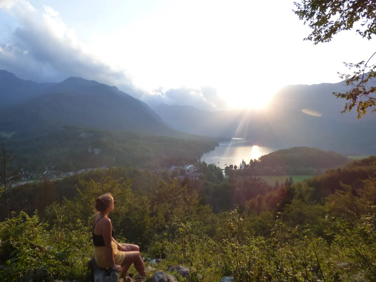 Femme assise sur un rocher devant le soleil couchant