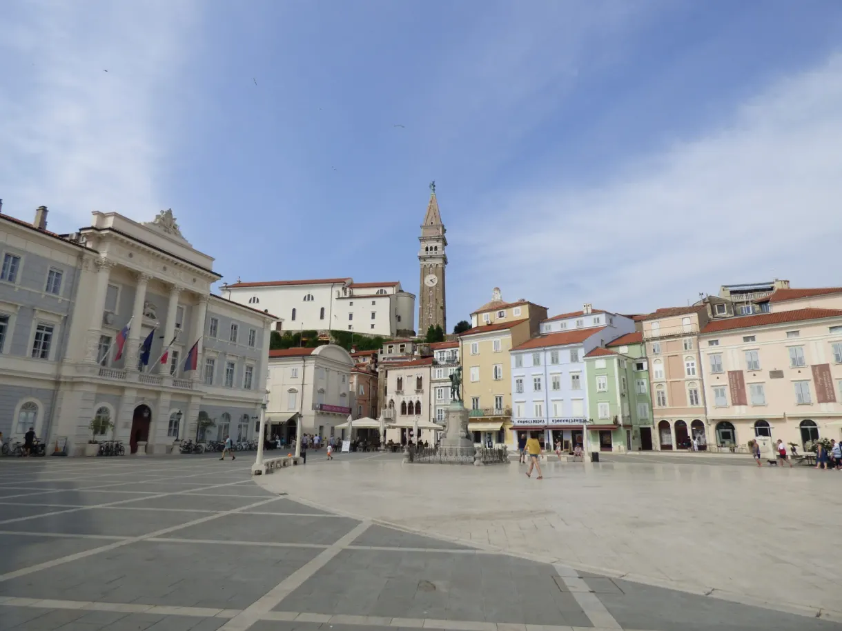 Vaste place ovale au dallage clair, bordée de façades colorées