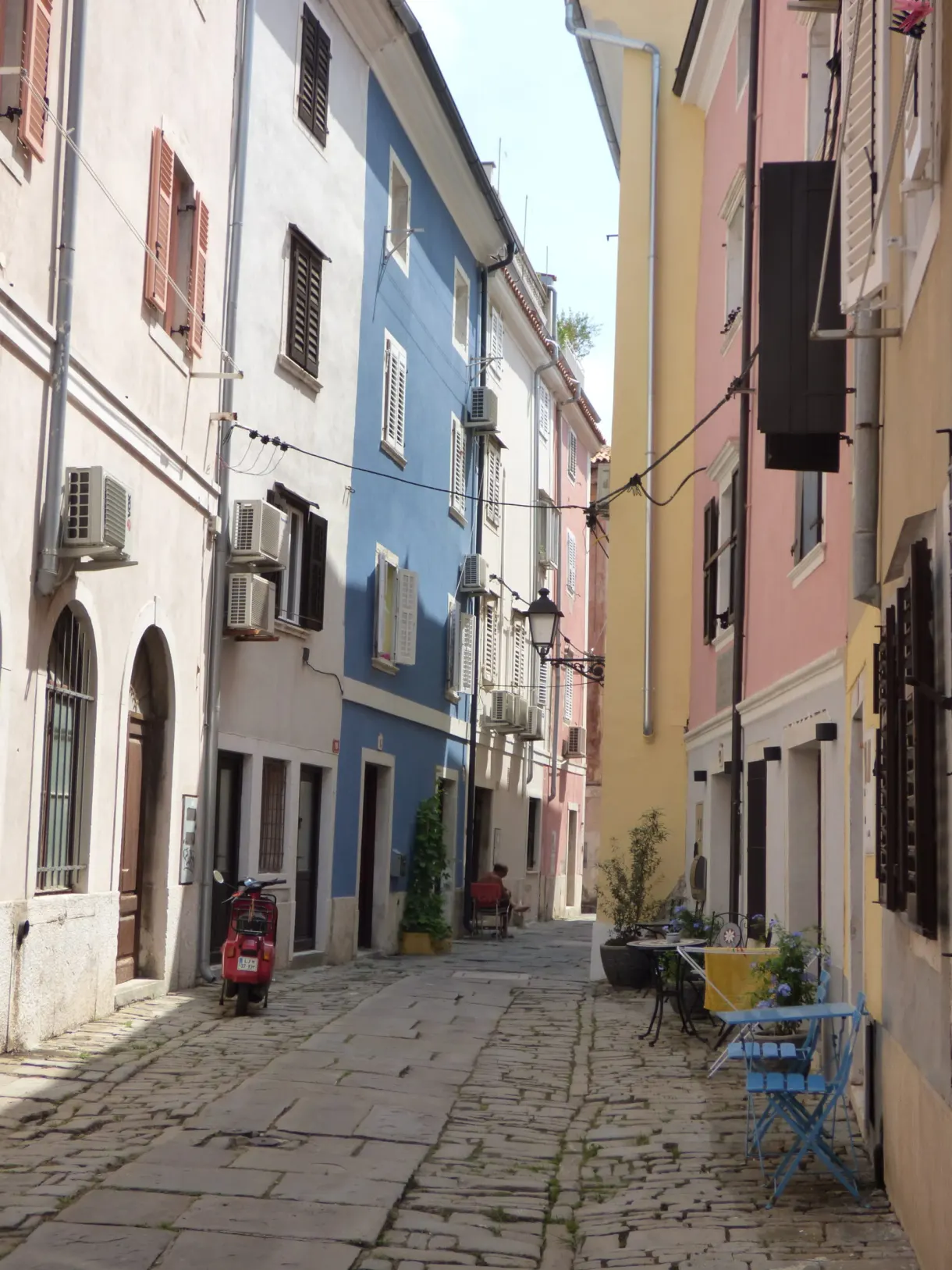 Ruelle pavée aux façades bleu et jaune, chaises de bistrot