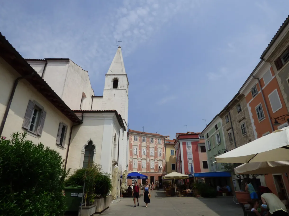 Église blanche et terrasses de café sur une place d'Izola