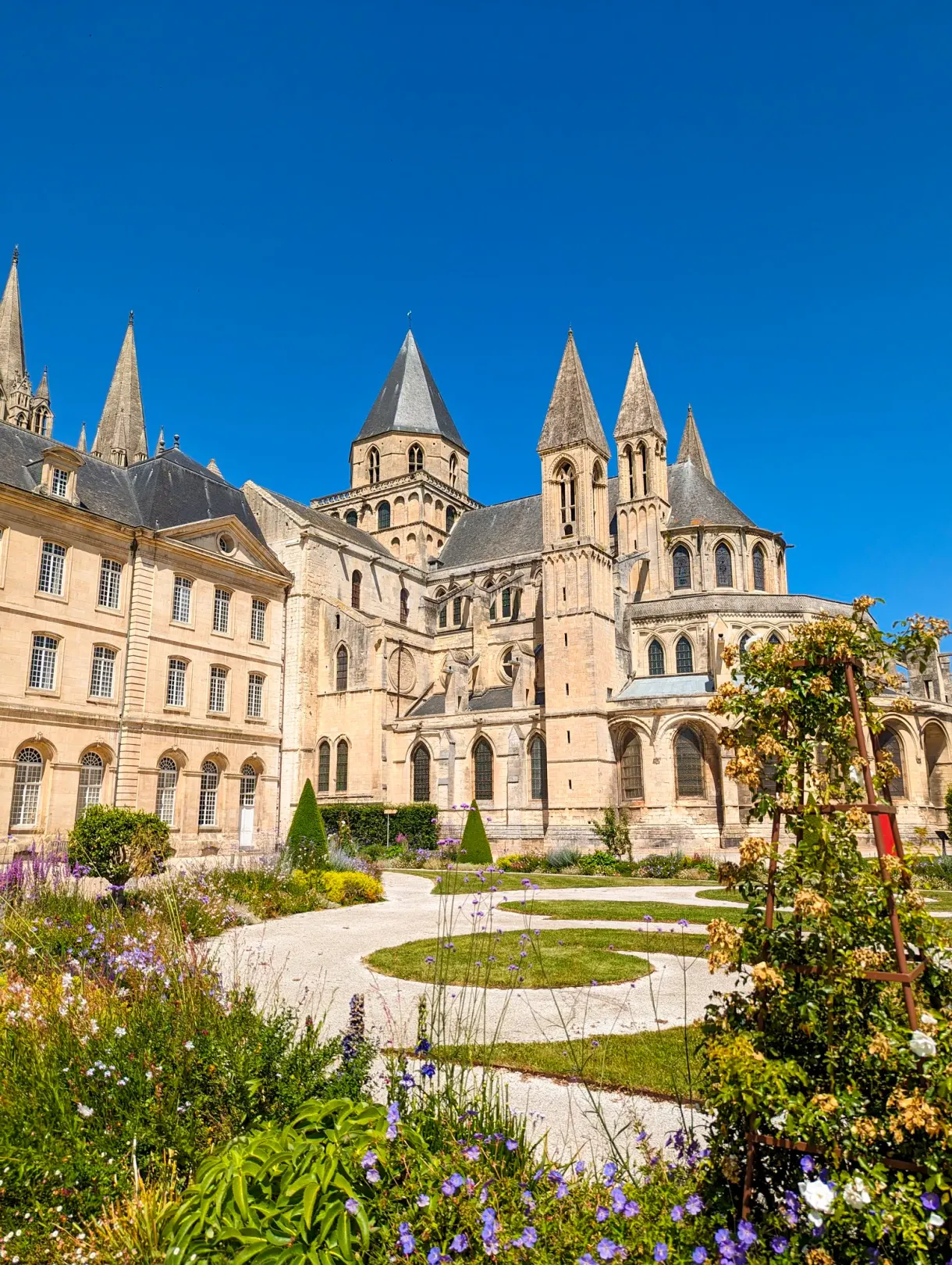 Abbaye aux Hommes et son jardin fleuri sous un ciel d'été