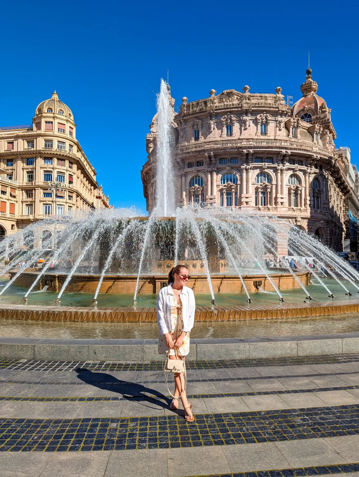 Femme en robe claire devant la grande fontaine de la place centrale