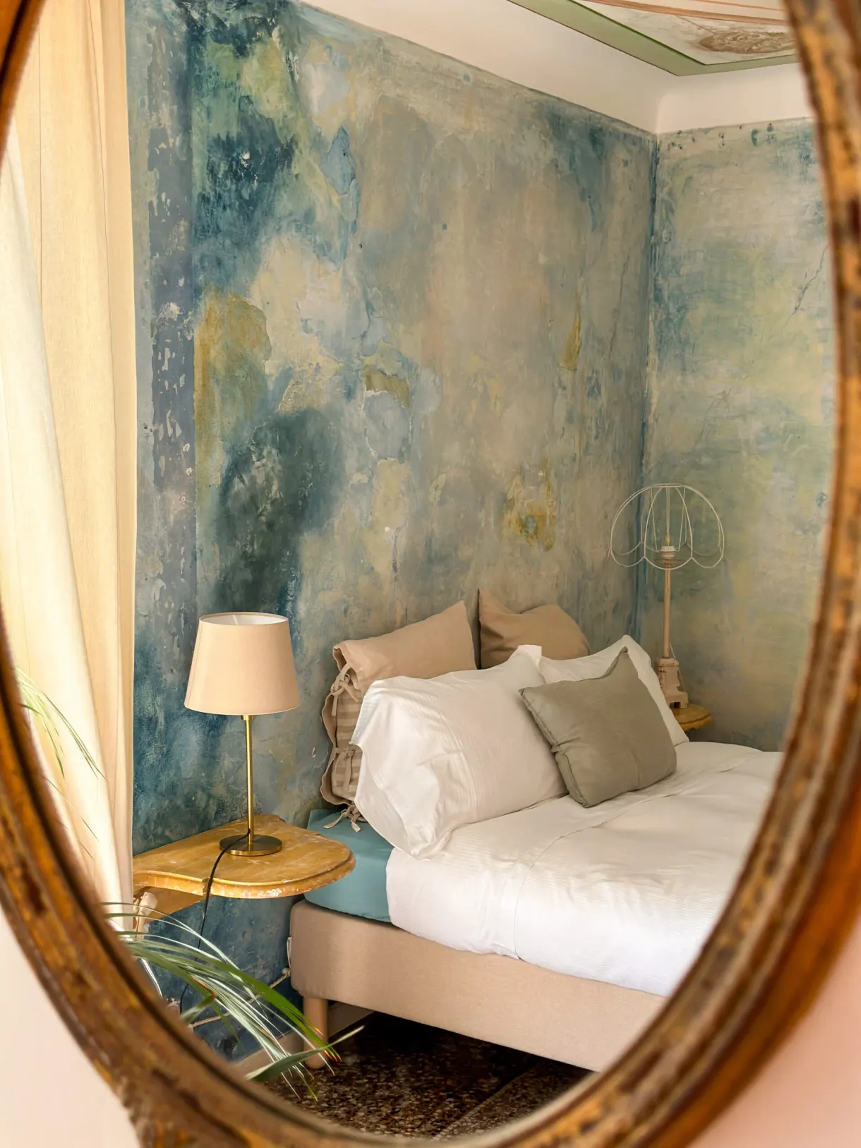 Chambre aux murs peints à fresque, vue dans un miroir doré, dans une maison d'hôtes partenaire