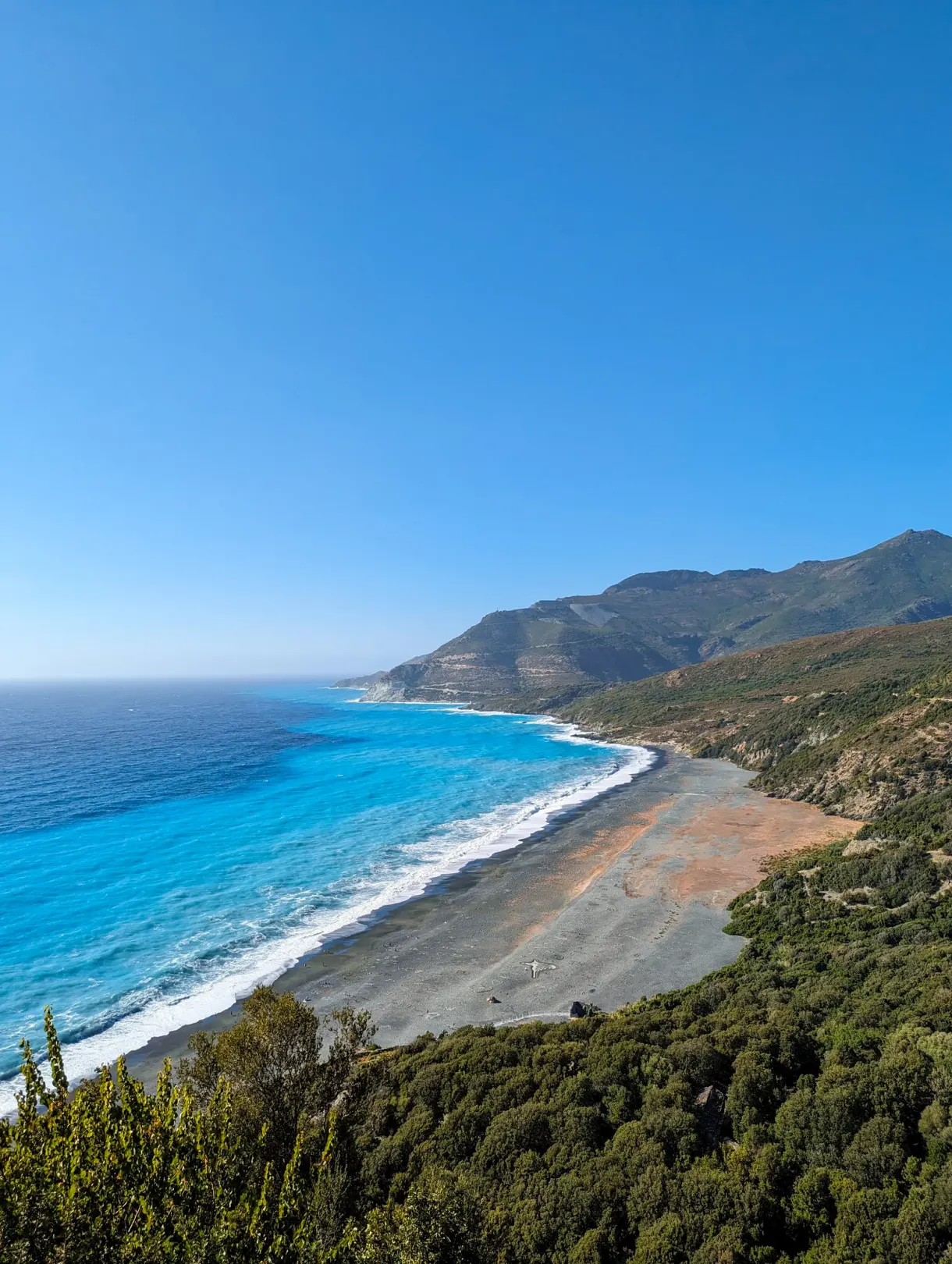 Plage de galets et eau turquoise au pied des reliefs corses