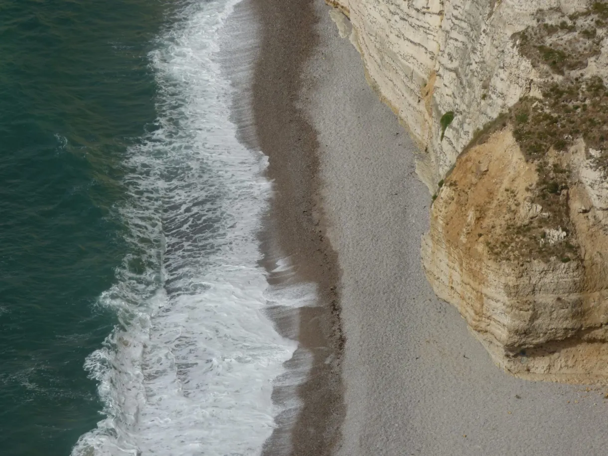 Vagues blanches déferlant sur le liseré de galets au pied des falaises