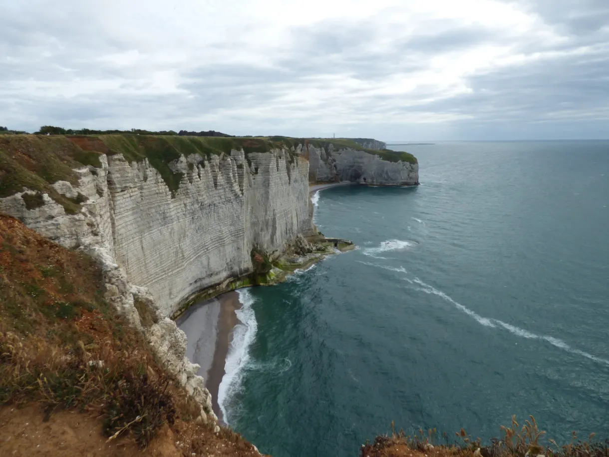 Falaises blanches déchiquetées et anse sombre sous un ciel gris