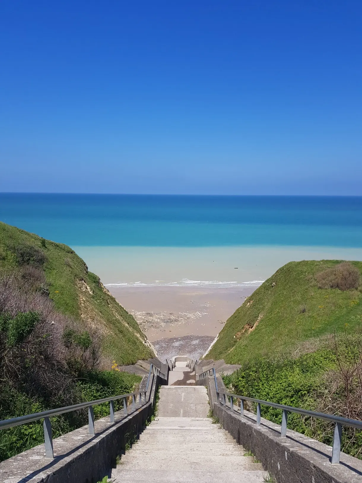 Escalier descendant vers la plage entre deux versants herbeux