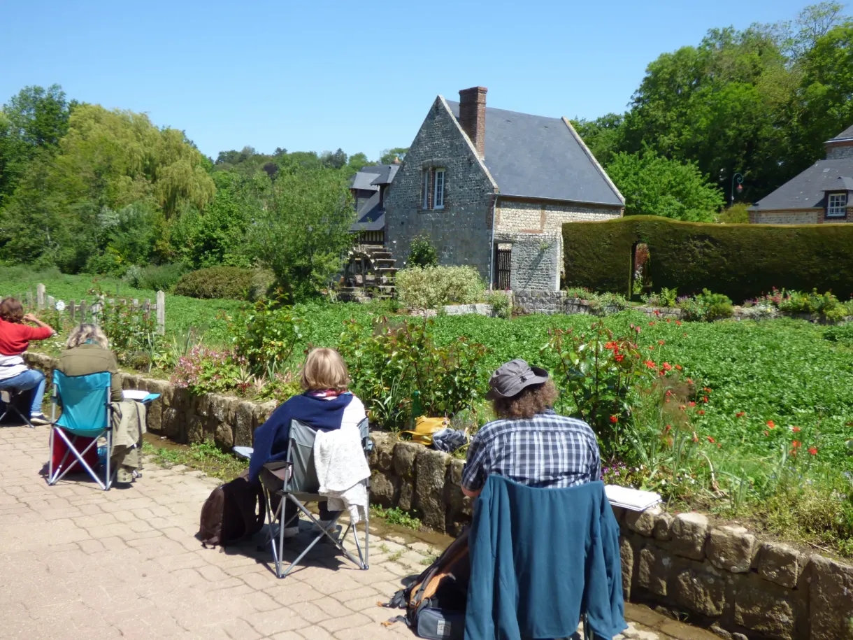Promeneurs installés au bord d'un jardin d'eau devant une maison de pierre